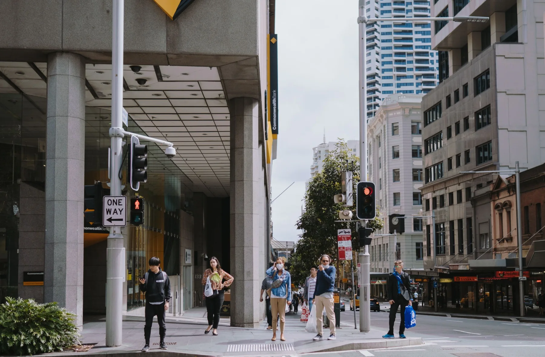 Pedestrians move through a city intersection beneath tall buildings.