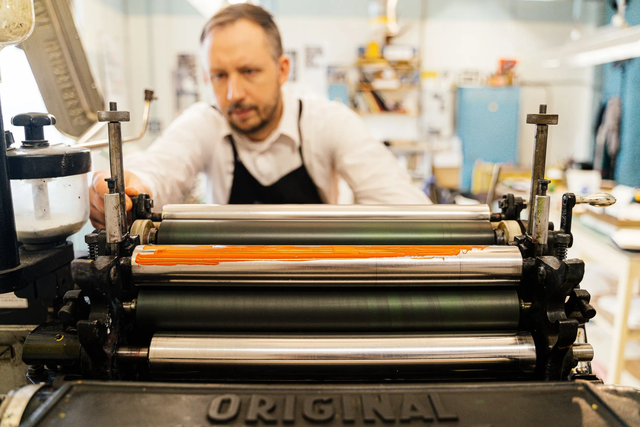 A printmaker operates a manual printing press in a workshop.