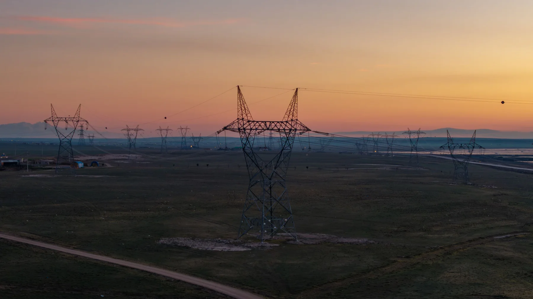 High-voltage transmission towers cross a broad landscape at dusk.