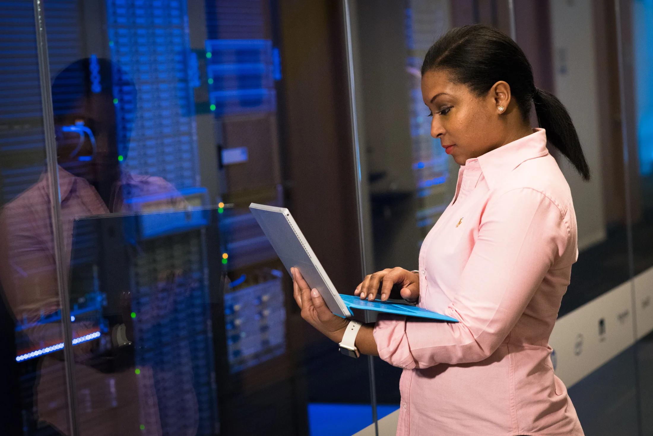 An engineer studies a tablet beside equipment in a server room.