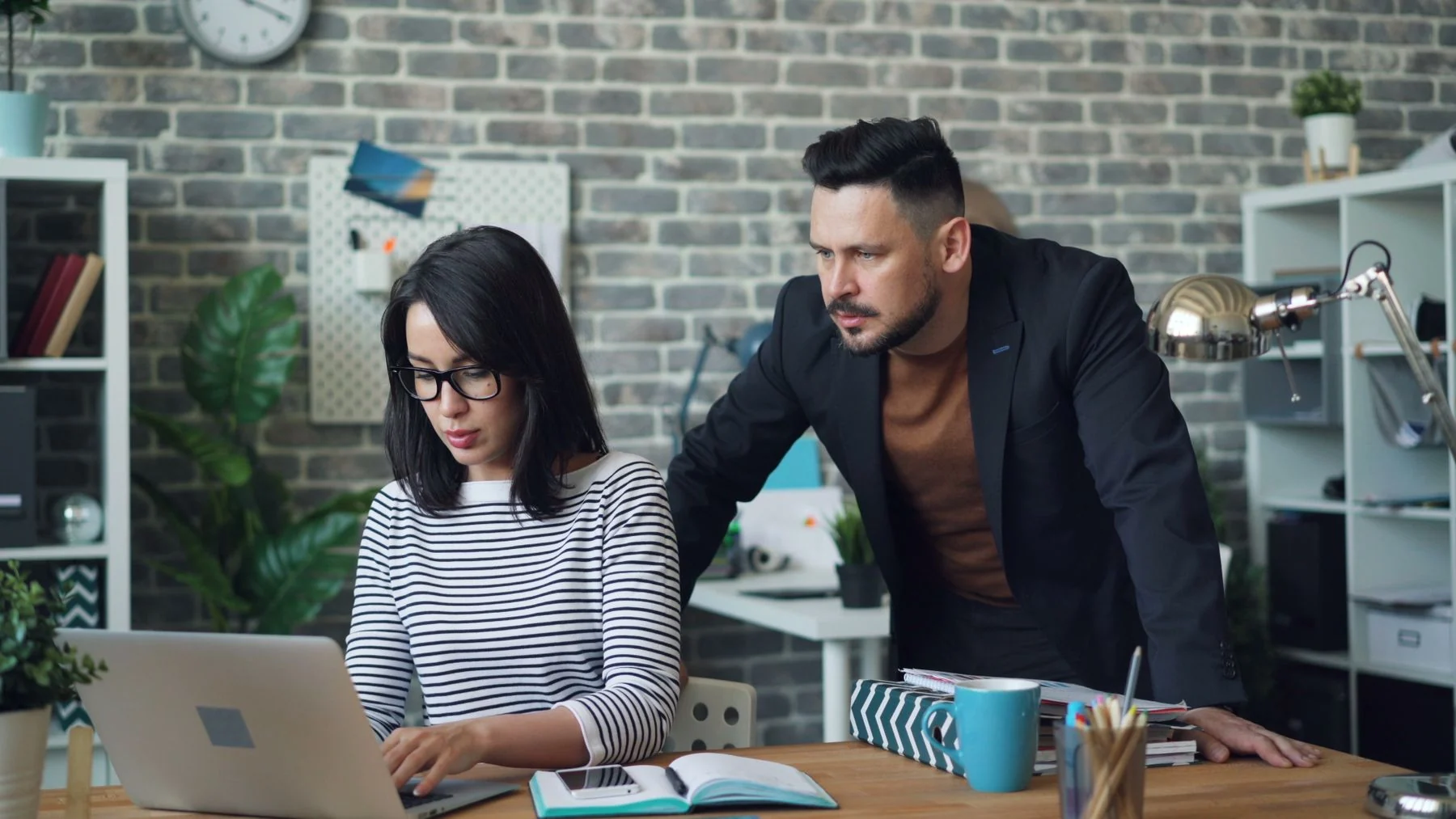 Two colleagues examine work together at a laptop.