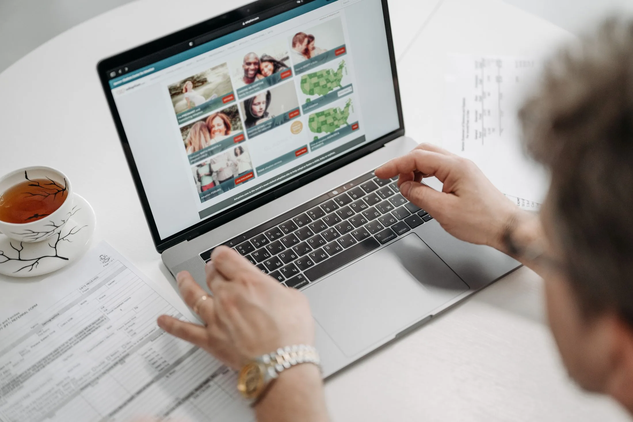 A person uses a laptop to browse a website while printed notes sit on the desk.