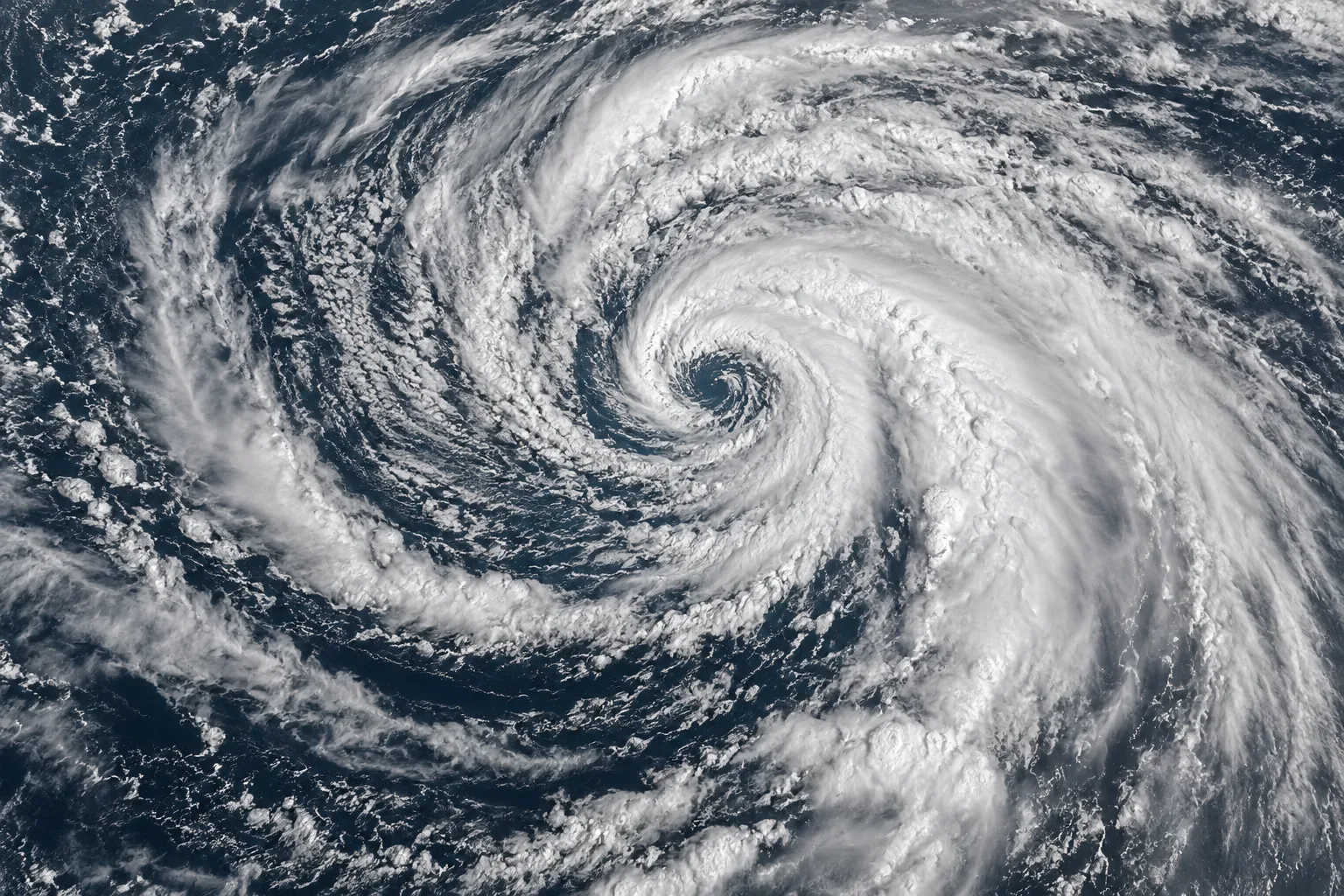 A vast spiral of cloud bands over a dark ocean, viewed from above.