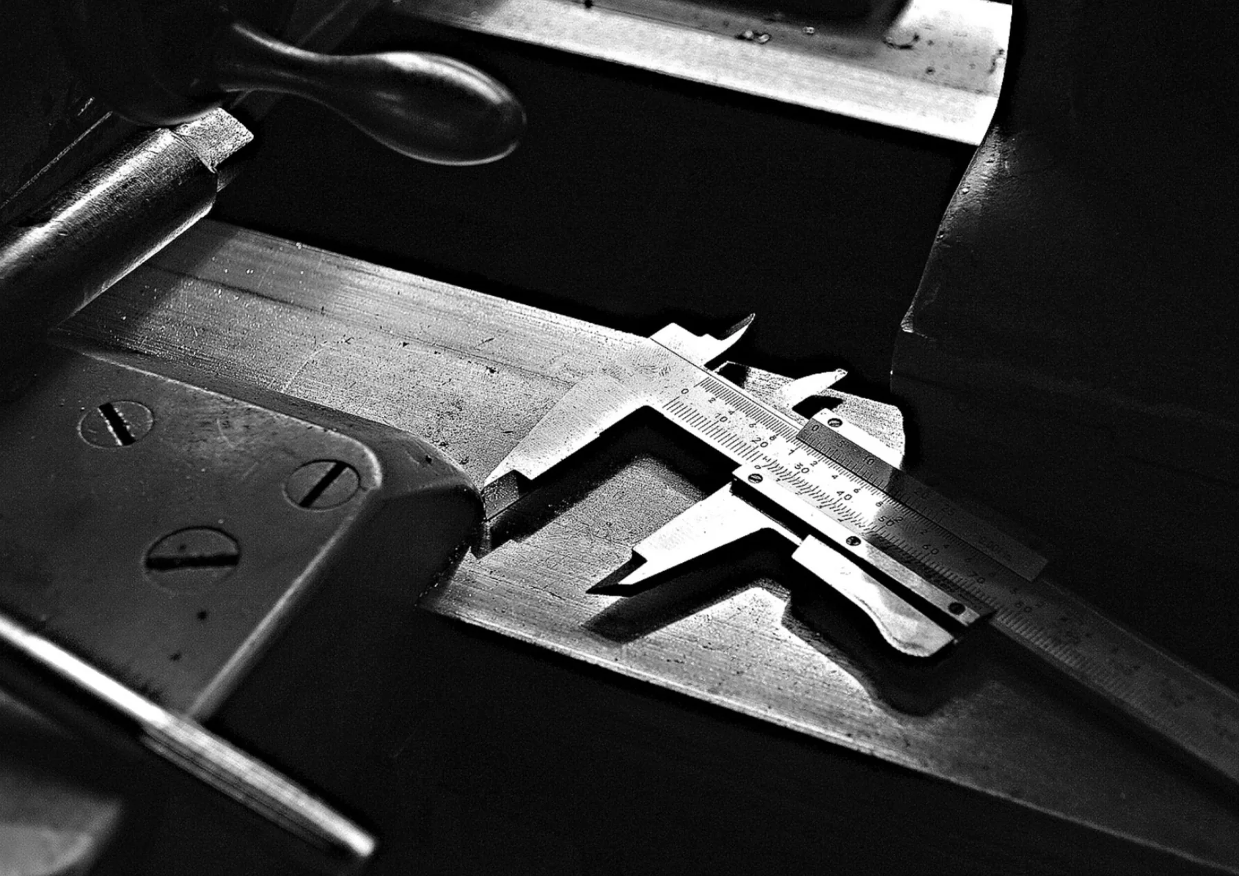 A metal caliper measures a piece of steel on a workbench.