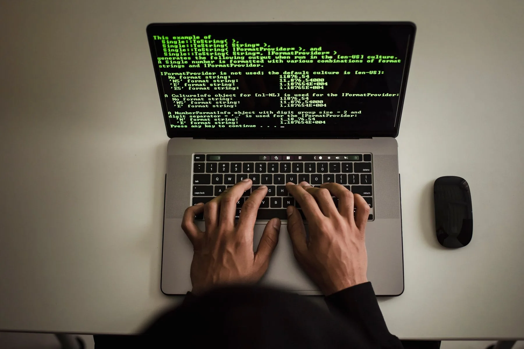 Hands typing on a laptop displaying programming code, viewed from above.