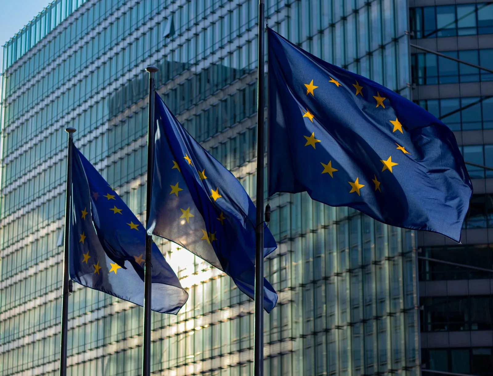 European Union flags outside a modern glass building in Brussels.