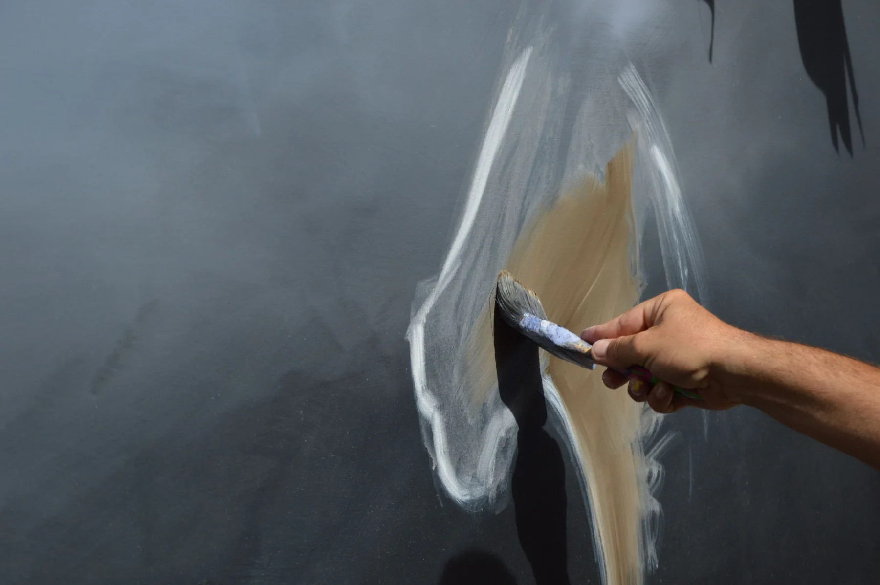 An artist paints a broad, expressive brushstroke across a canvas.