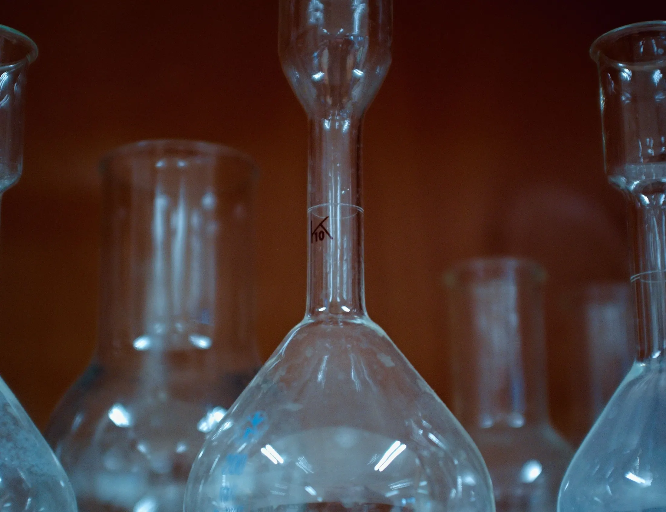 Glass laboratory flasks in a dim room, with a central flask sharply lit against softer shapes.