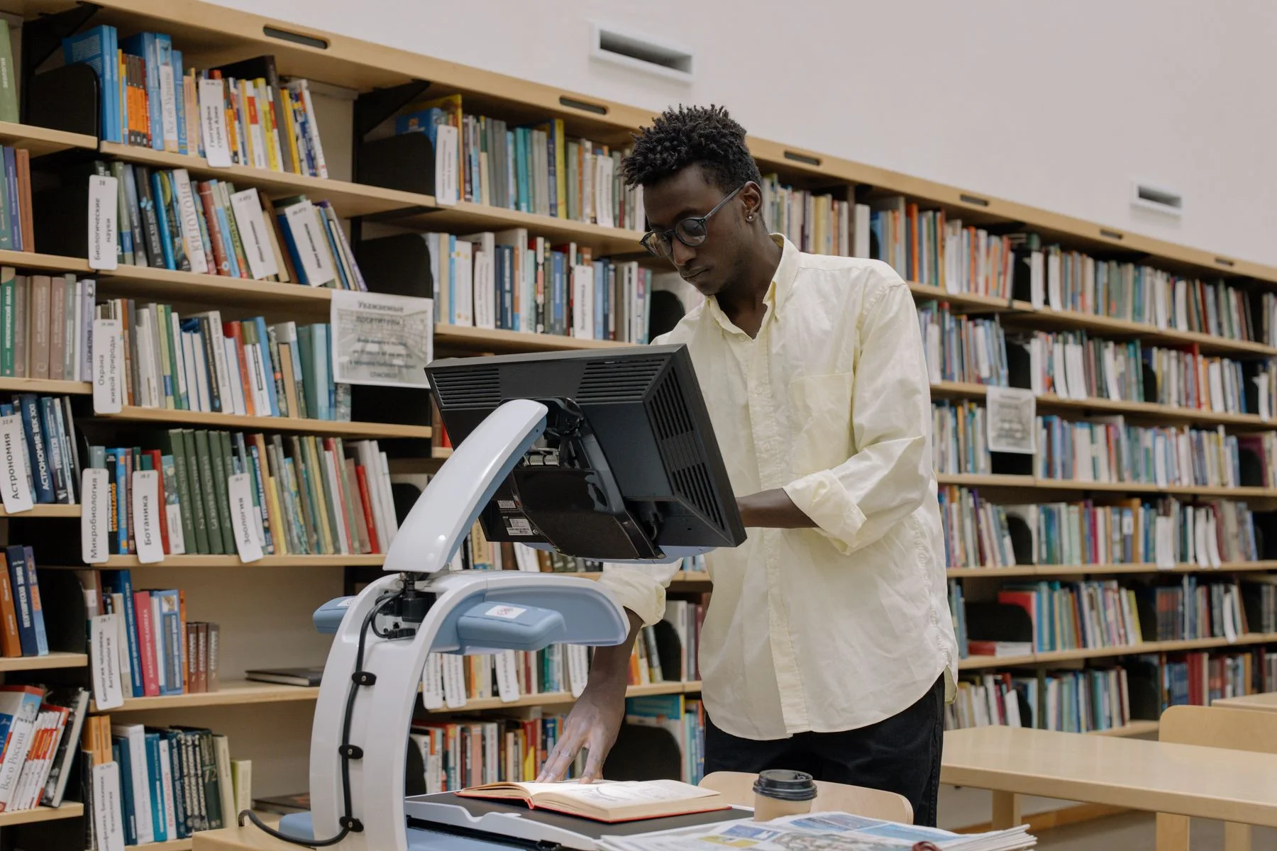 A researcher digitizes an open book in a library surrounded by shelves.