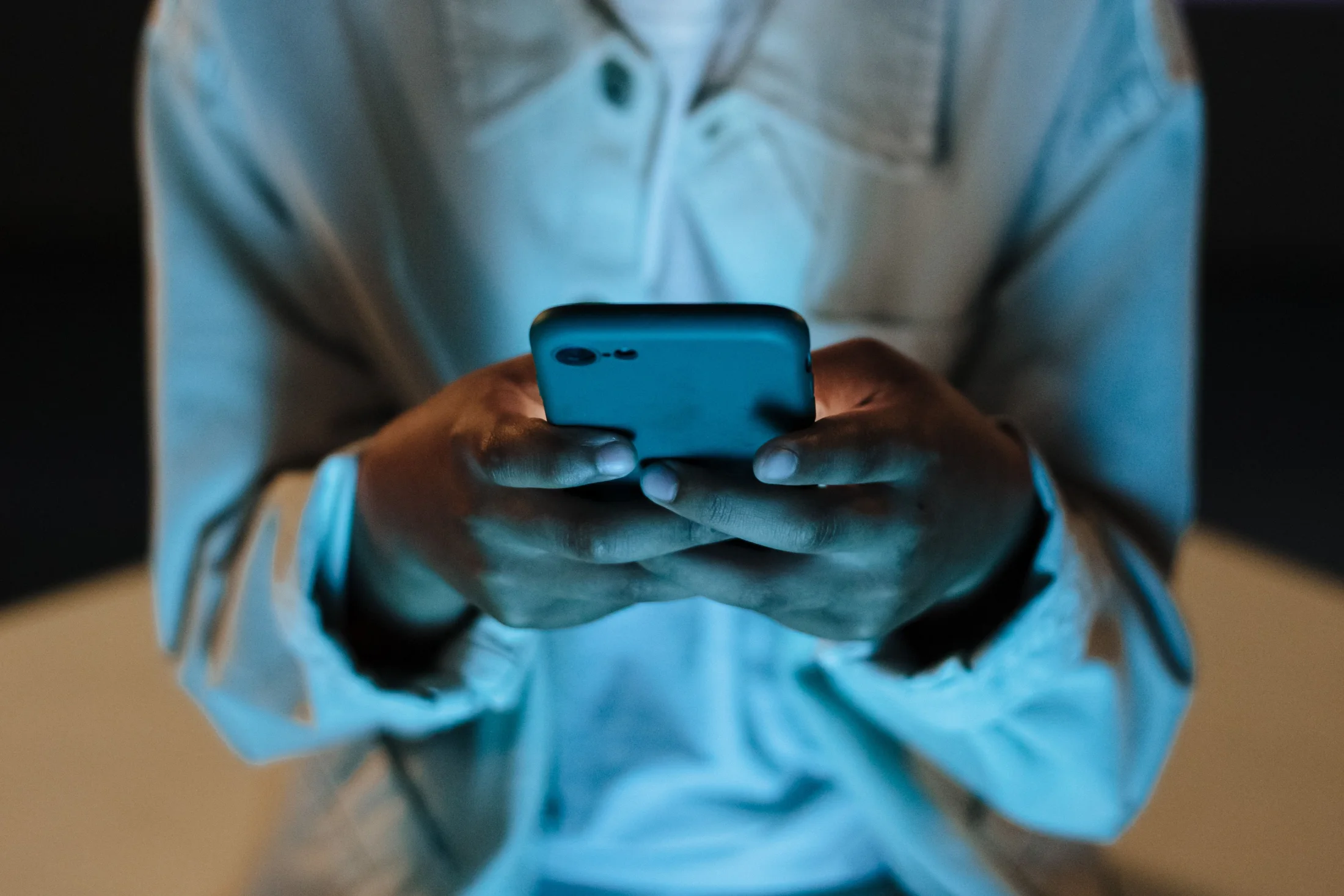 A person holds and uses a smartphone in a dim indoor setting.