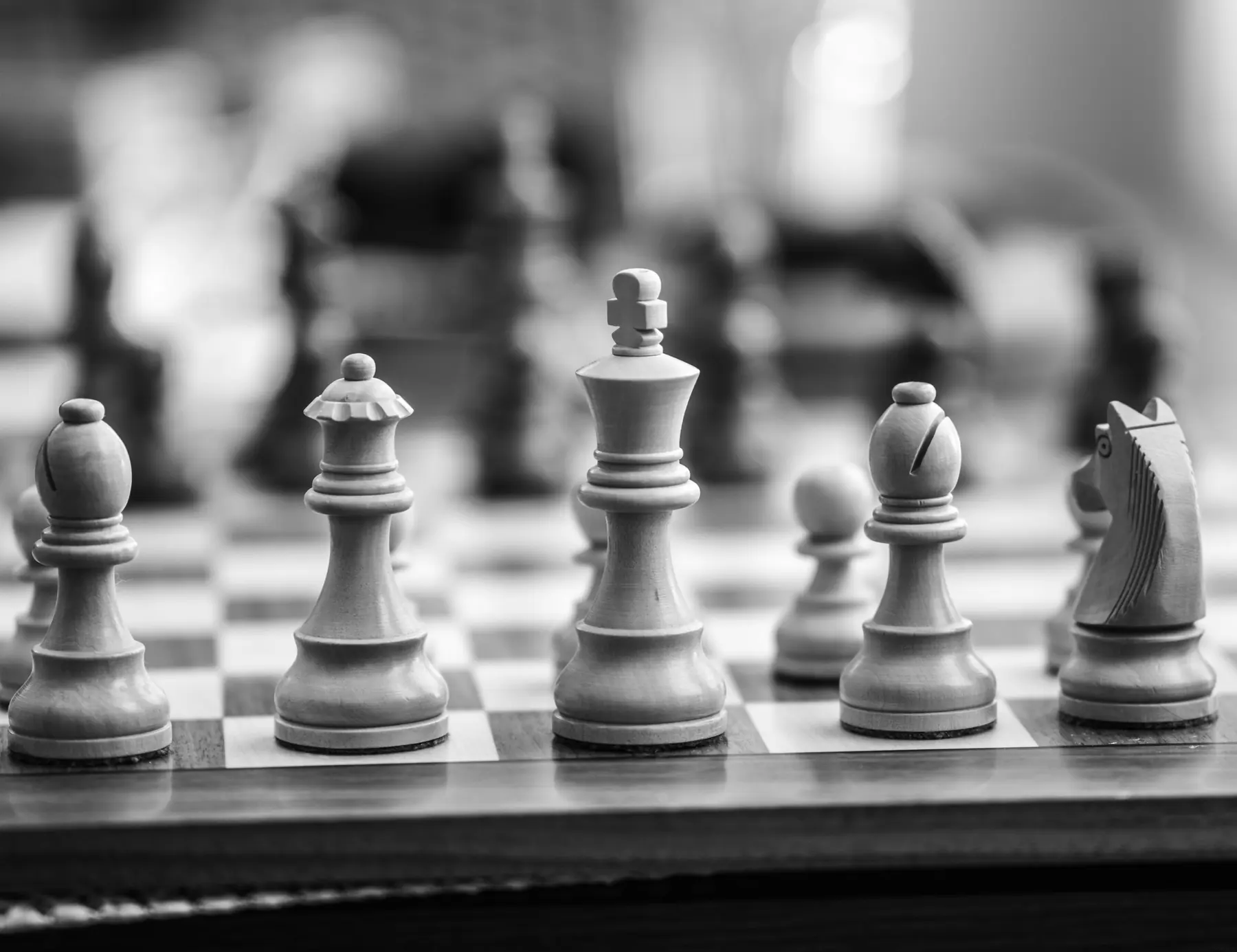 Black and white chess pieces in a row, with the center king in focus and the surrounding pieces softly blurred.