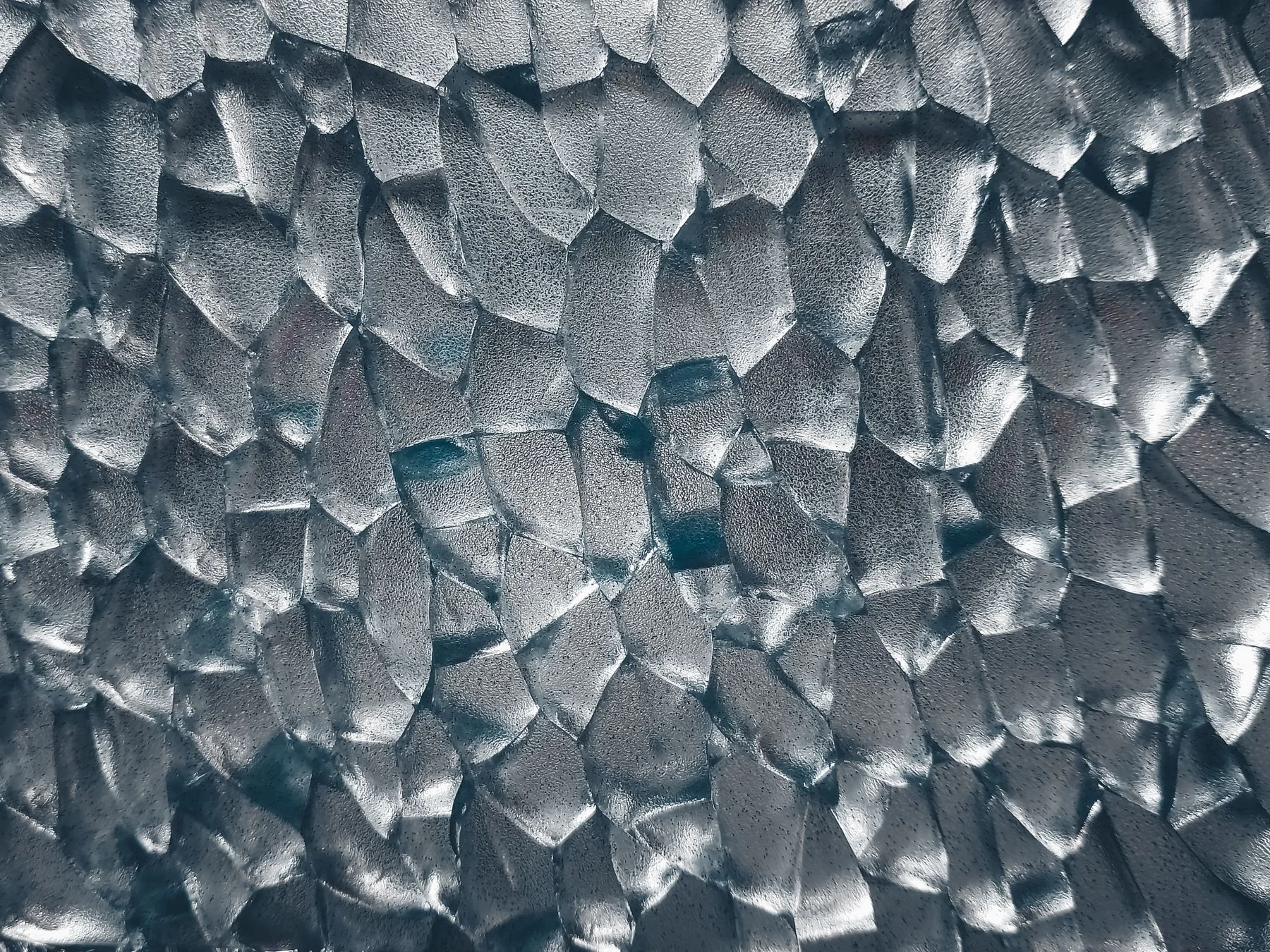 A close-up photograph of overlapping textured glass forms in soft gray light.